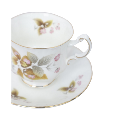 Een wit porseleinen theekopje met schoteltje, versierd met delicate herfstbladeren en kleine roze bloemen.
