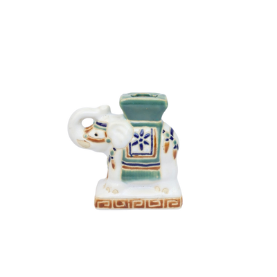 Een kleine, witte keramische olifant met groene accenten, een blauw bloemenmotief en een decoratieve voet.
