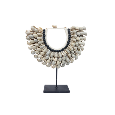 Een decoratieve halsketting van kauri schelpen met zwarte kralen op een zwarte metalen standaard.