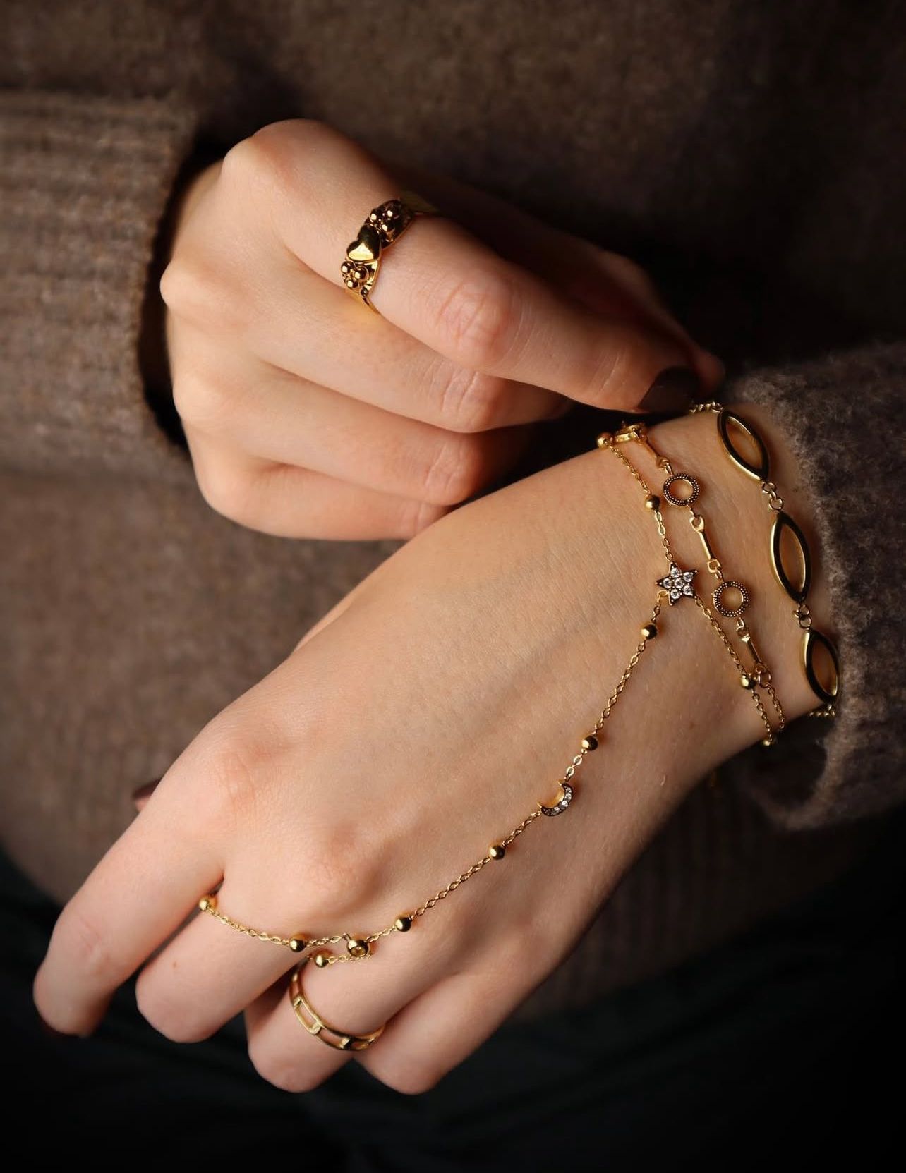 Een persoon draagt ​​gouden ringen en een ingewikkelde, armband met delicate kralen en een klein, fonkelend steentje.