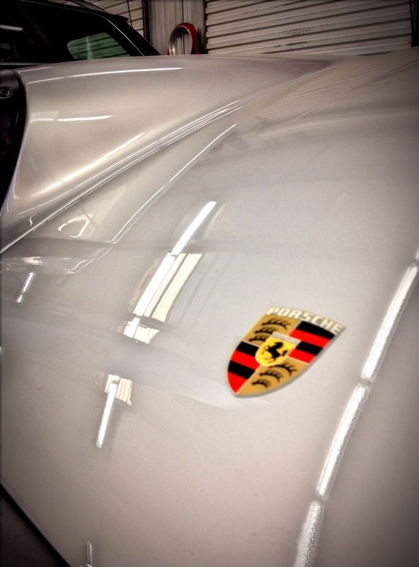 White Porsche hood with emblem and reflected lights in a garage