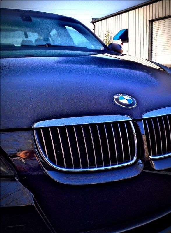 Close-up of a black BMW hood and grille with blue paint reflections, parked outdoors