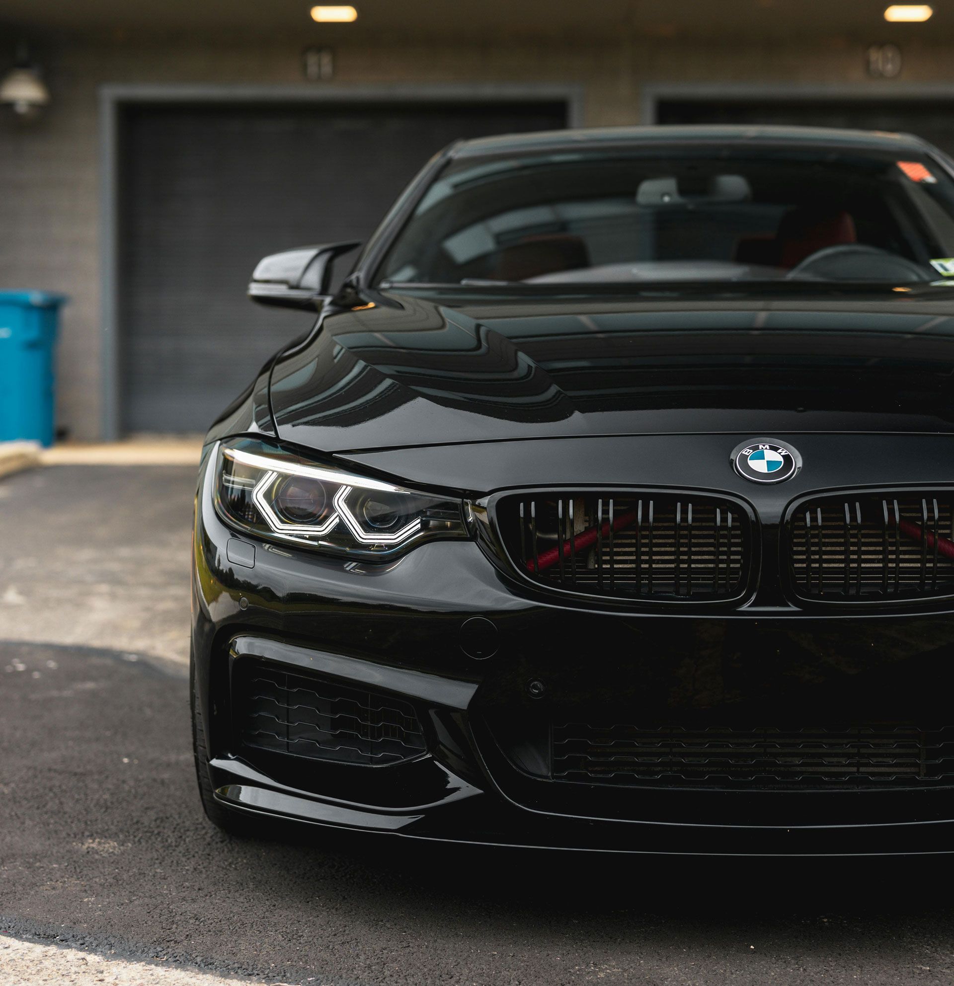 Black BMW sports car parked in a garage, front view with headlights on