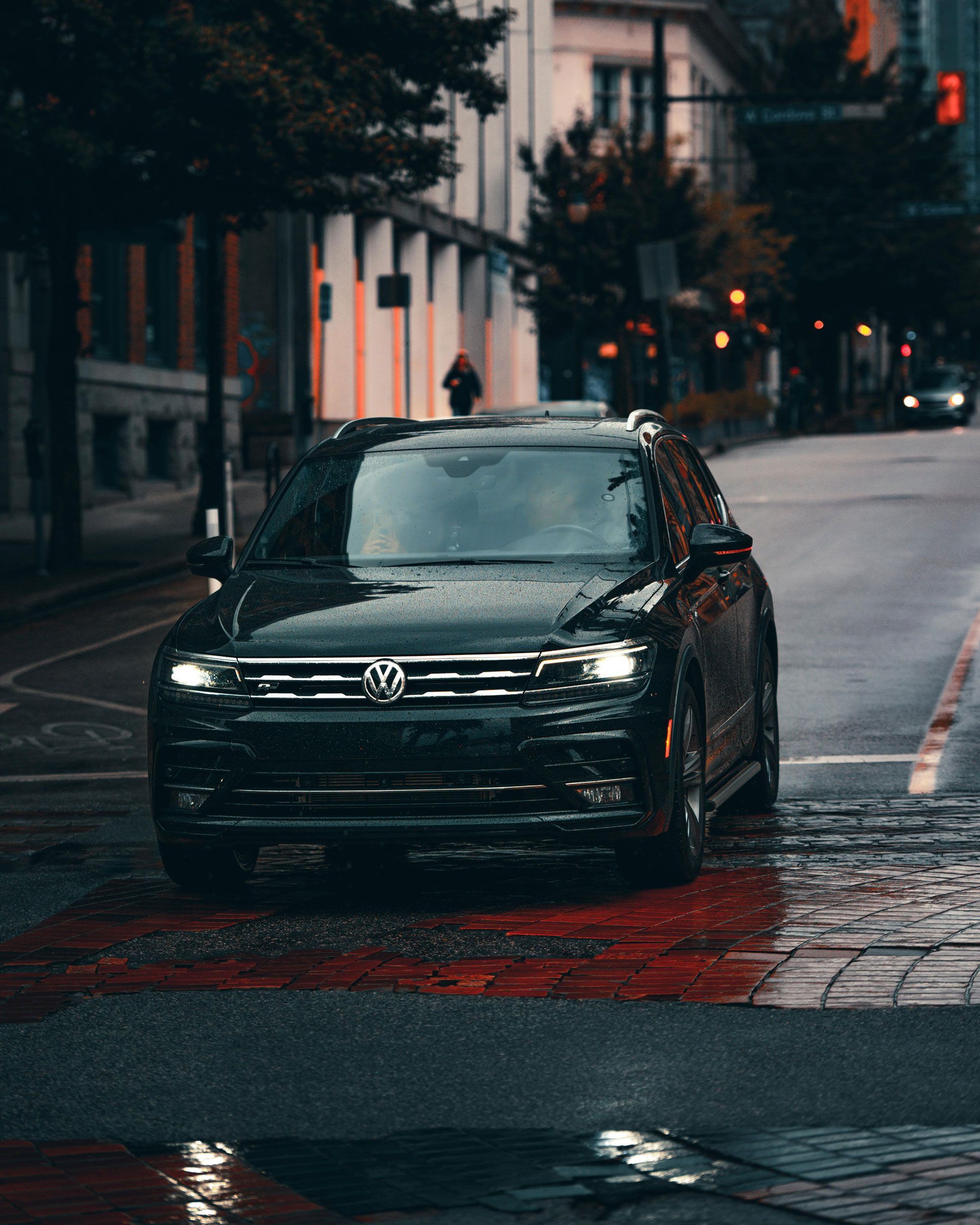 Black Volkswagen driving on a wet city street at dusk with reflections on the pavement