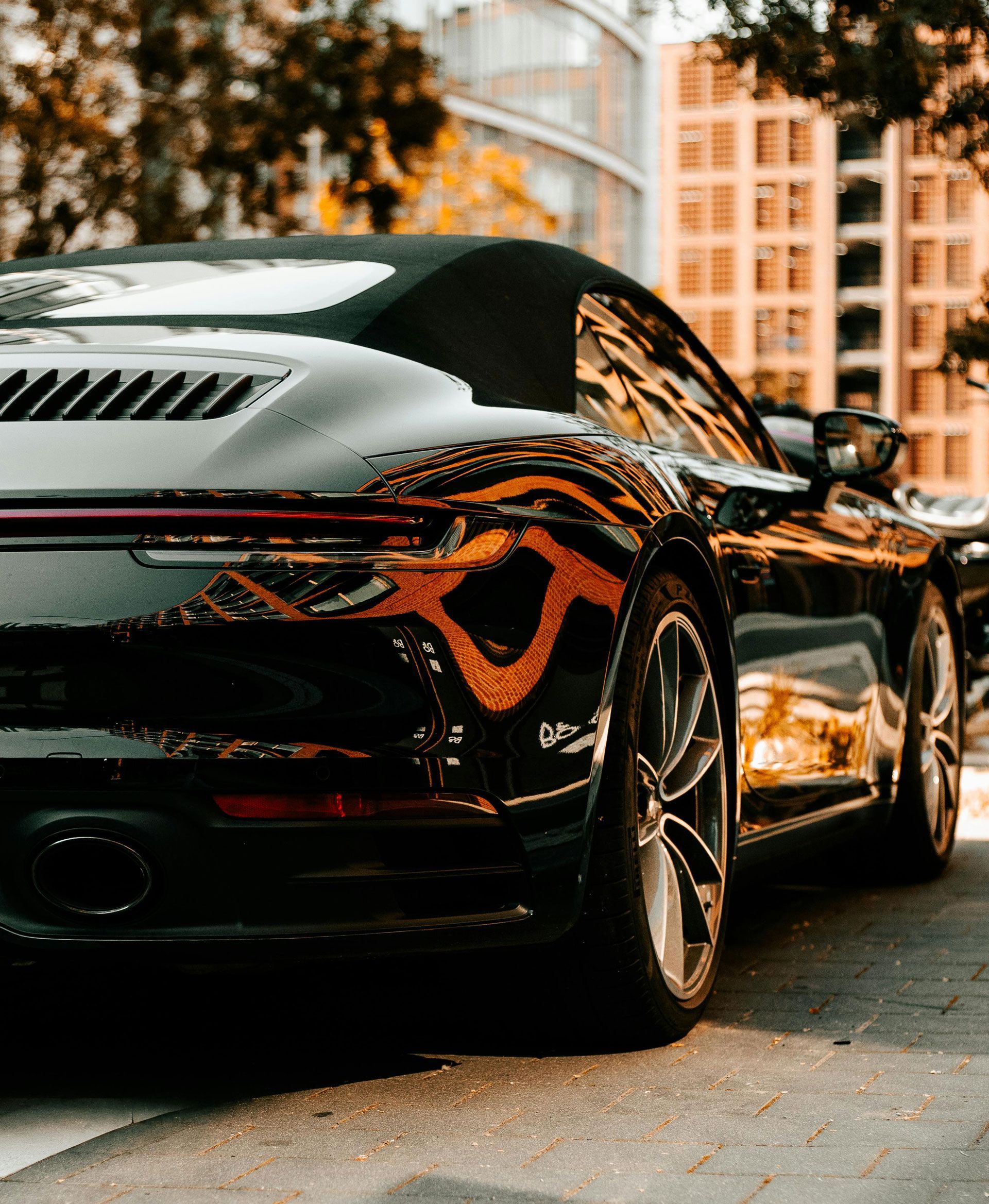 Black sports car parked on a city street, viewed from the rear at sunset