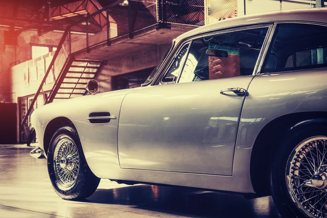 Silver classic car parked in a warm-lit garage, side view with chrome wire wheels