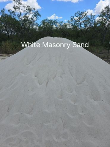 Pile of white masonry sand against a background of trees and a blue sky.