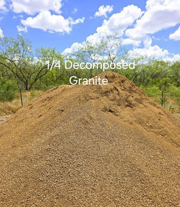 Pile of tan decomposed granite under a blue sky with clouds, trees in the background.