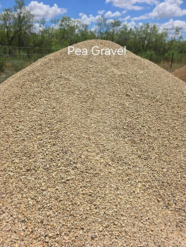 Pile of pea gravel in a yard against a background of trees and a partly cloudy sky.