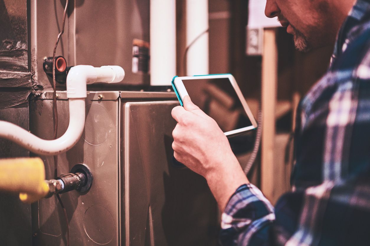 The Clean Air Act Technician is looking at a tablet while working on a heating system.