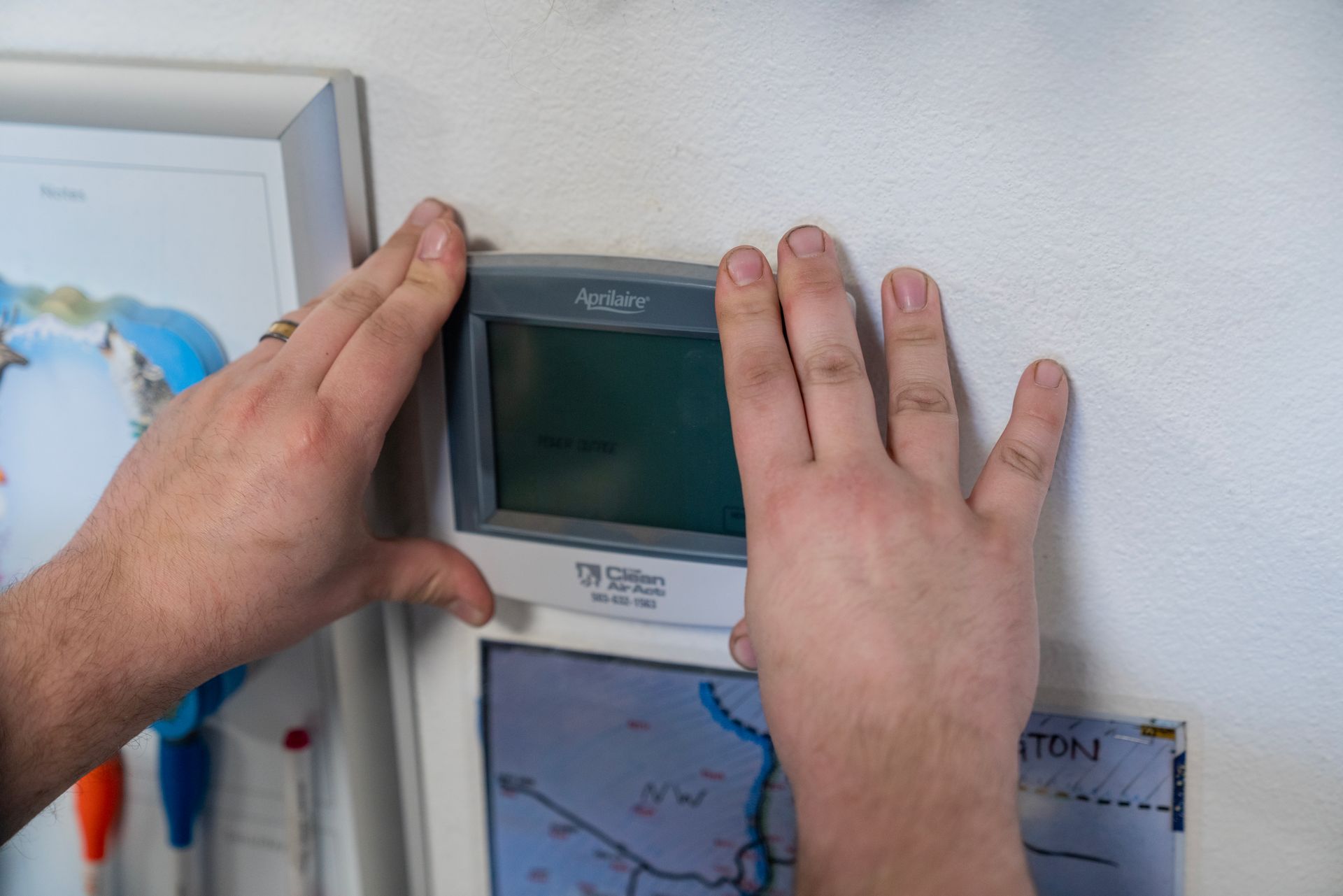 A person is adjusting a digital thermostat on a wall.