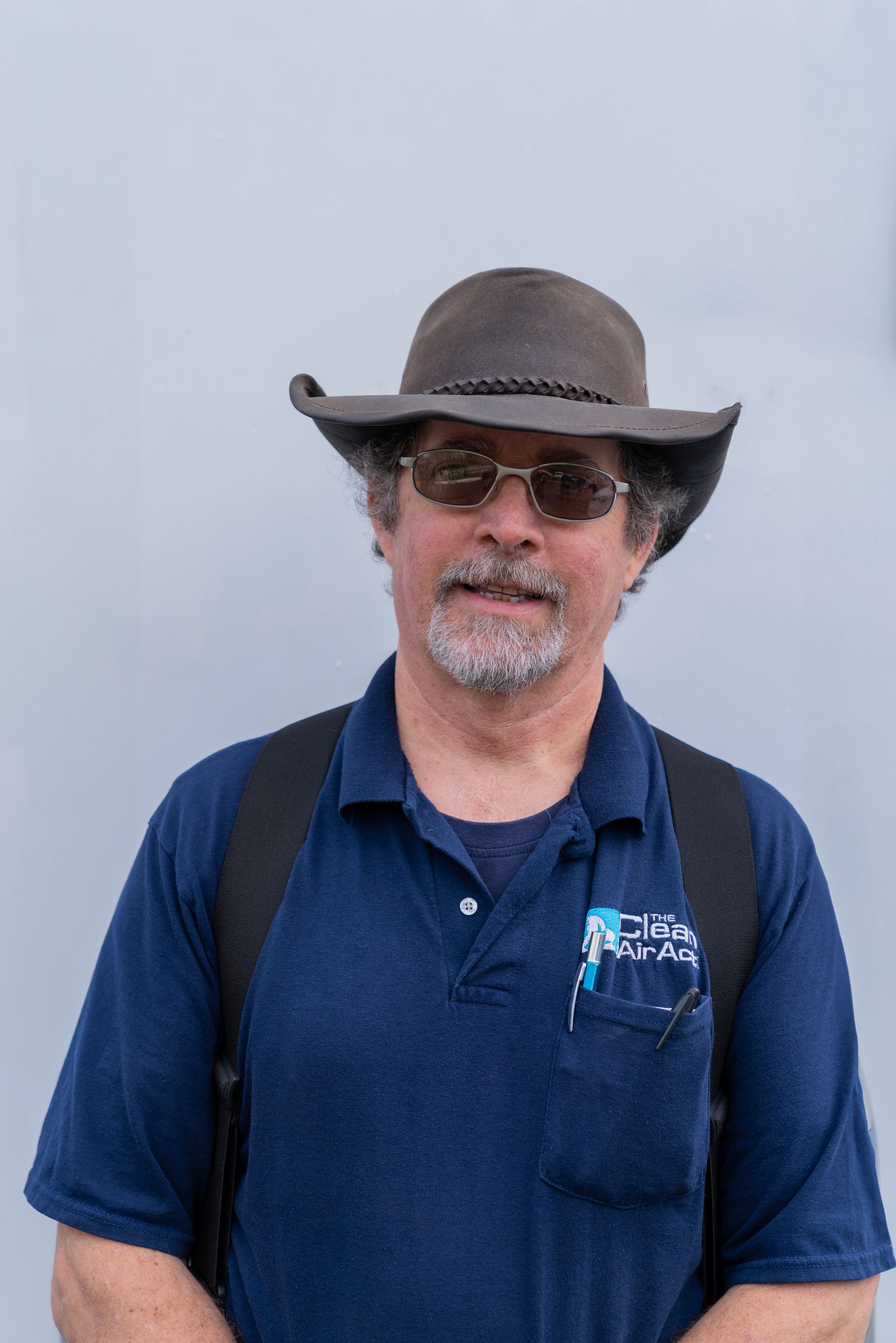 The Clean Air Act Technician wearing a cowboy hat and sunglasses is standing in front of a white wall.