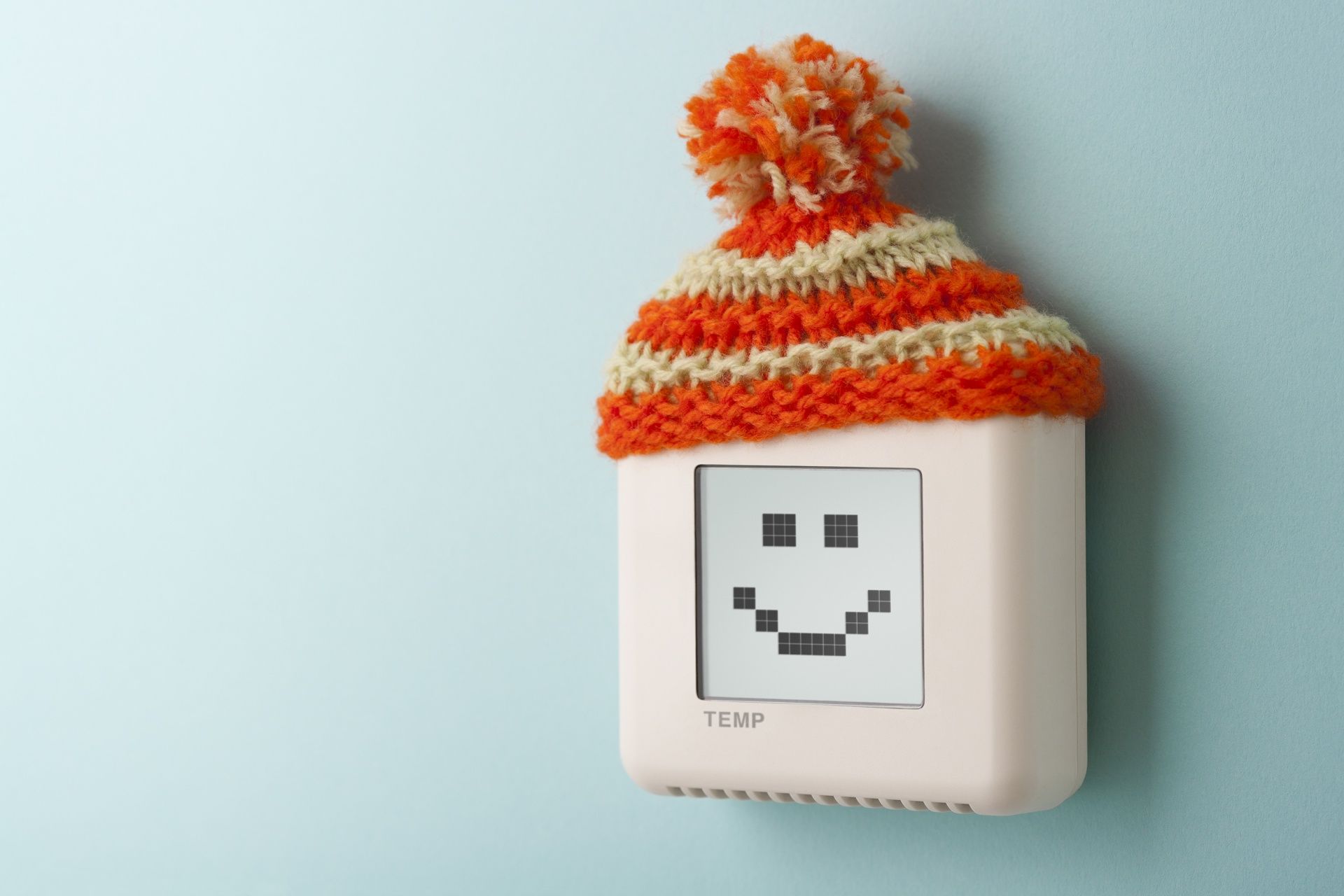 A thermostat with a smiley face on it is wearing a knitted hat.