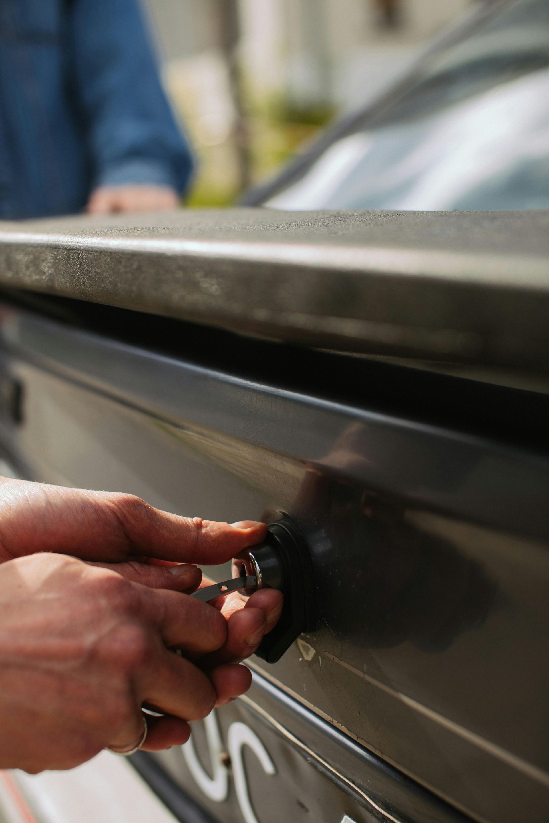 Hands using a key to unlock a black car trunk