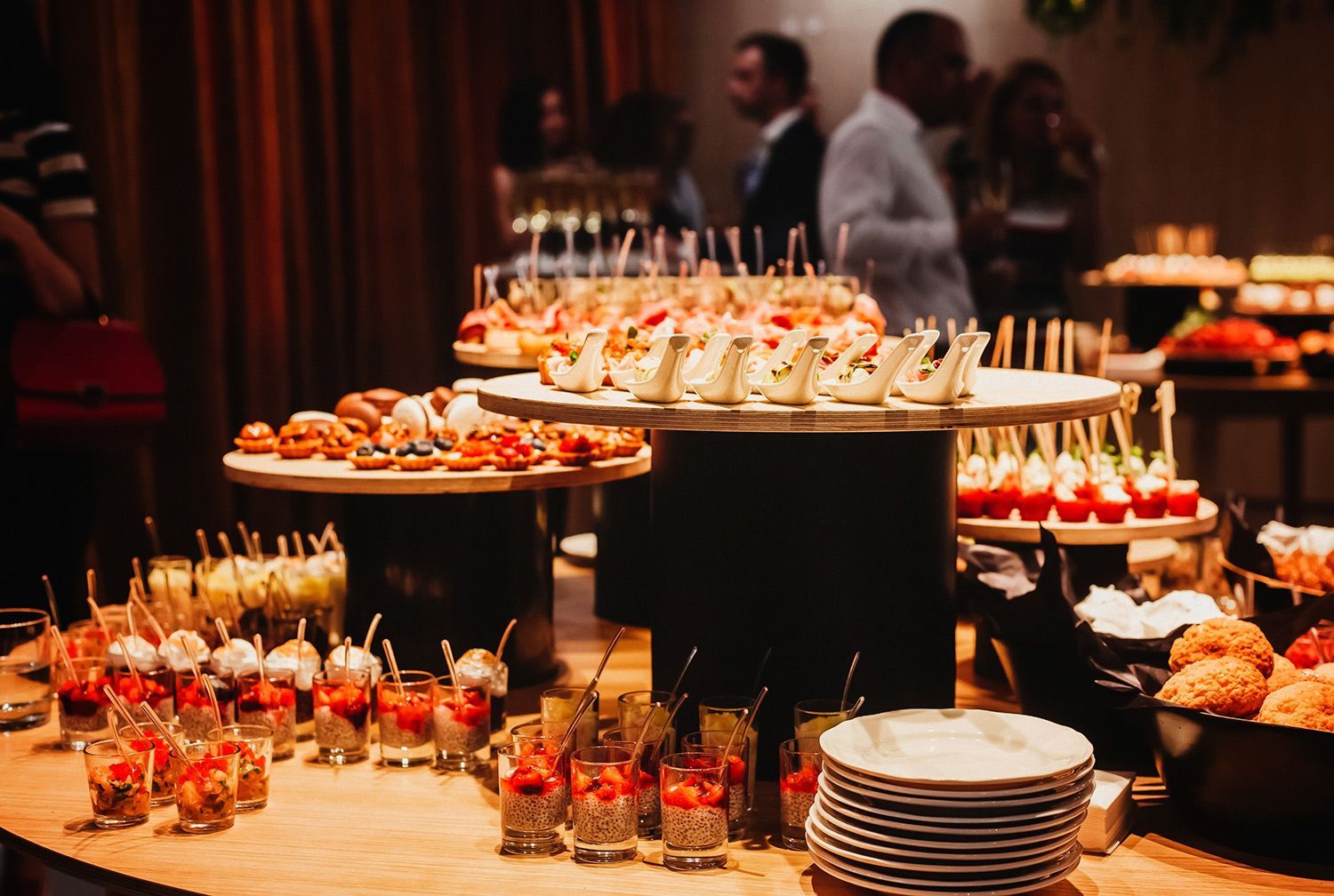 People serving a buffet of assorted hot dishes in stainless steel trays