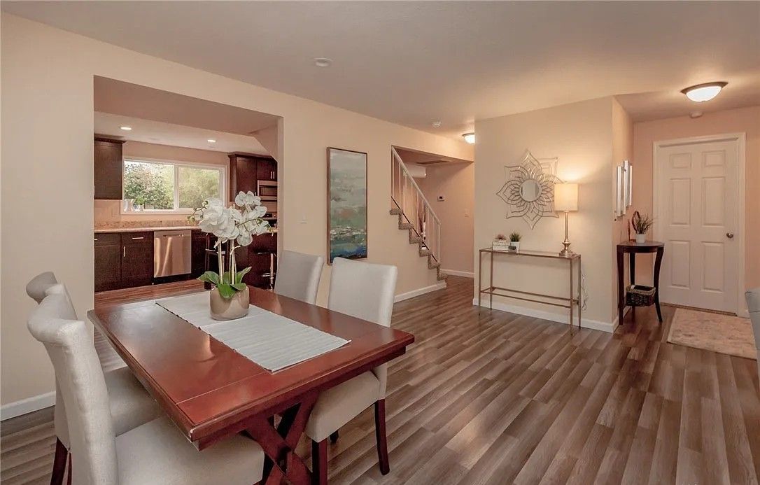 Dining room with wood table, four chairs, leading to kitchen and entryway with stairs.