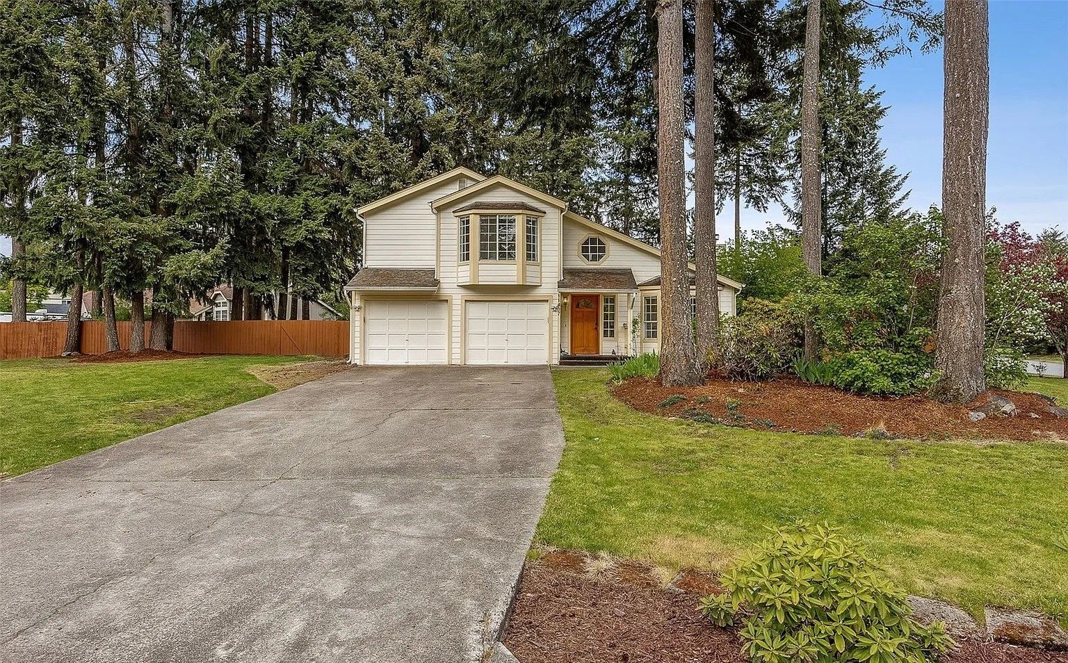 House with two-car garage, driveway, and tall trees in a suburban yard
