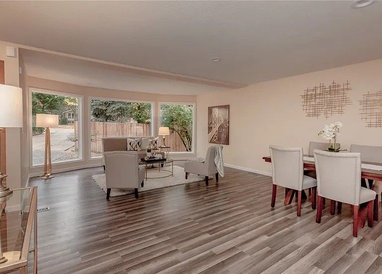 Open-concept living and dining area with large windows, light gray chairs, and a dark wood dining table.