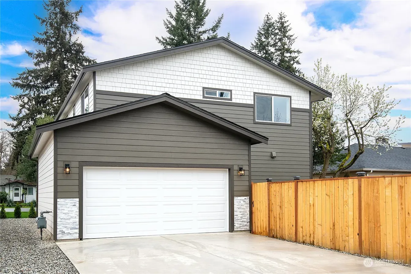 Modern two-story house with a white garage door, gray siding, and a wooden fence.