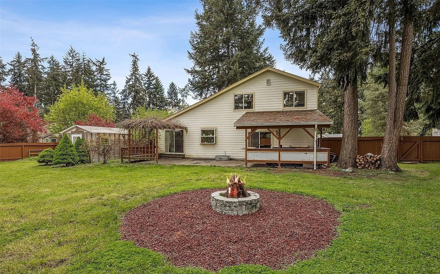 House with a covered porch and small fire pit in a green backyard with trees