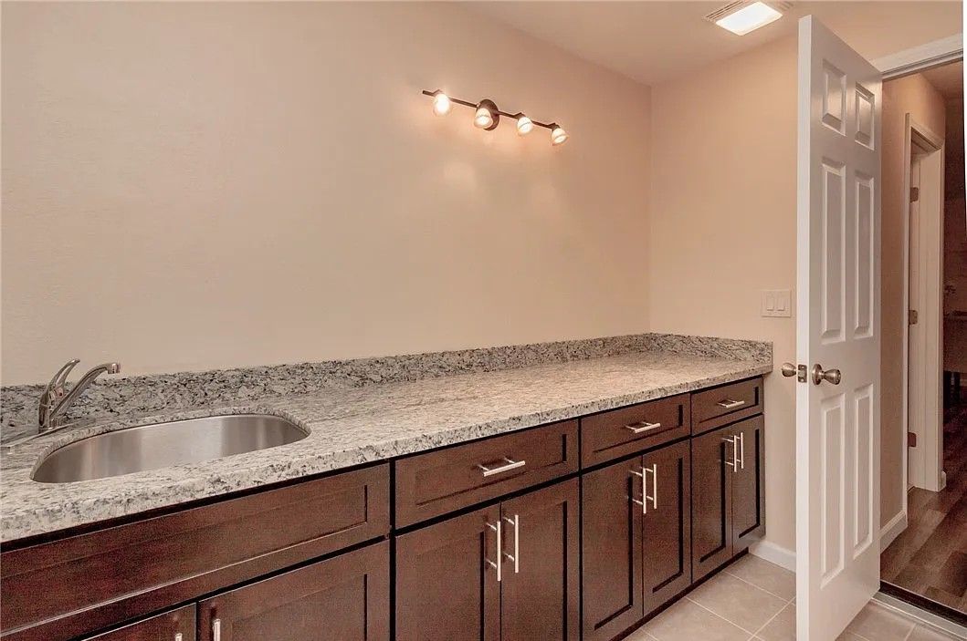 Dark brown cabinets with granite countertop and stainless steel sink. Open white door.