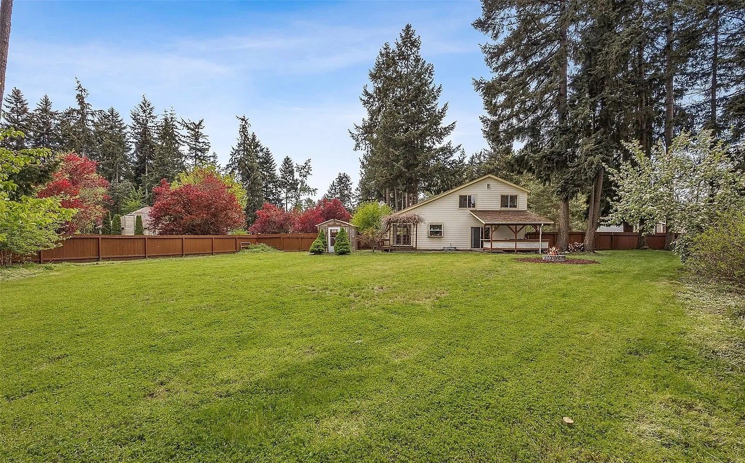 Large grassy backyard with trees and a small house under a clear sky
