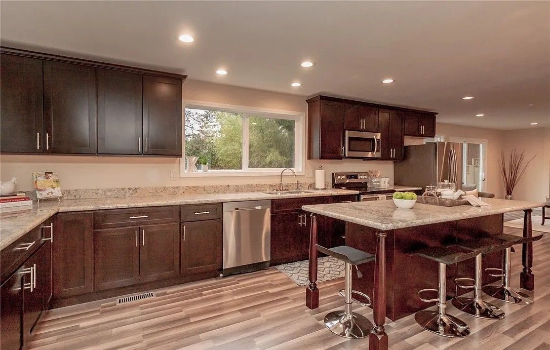 Modern kitchen with dark brown cabinets, stainless steel appliances, and a granite island with stools.