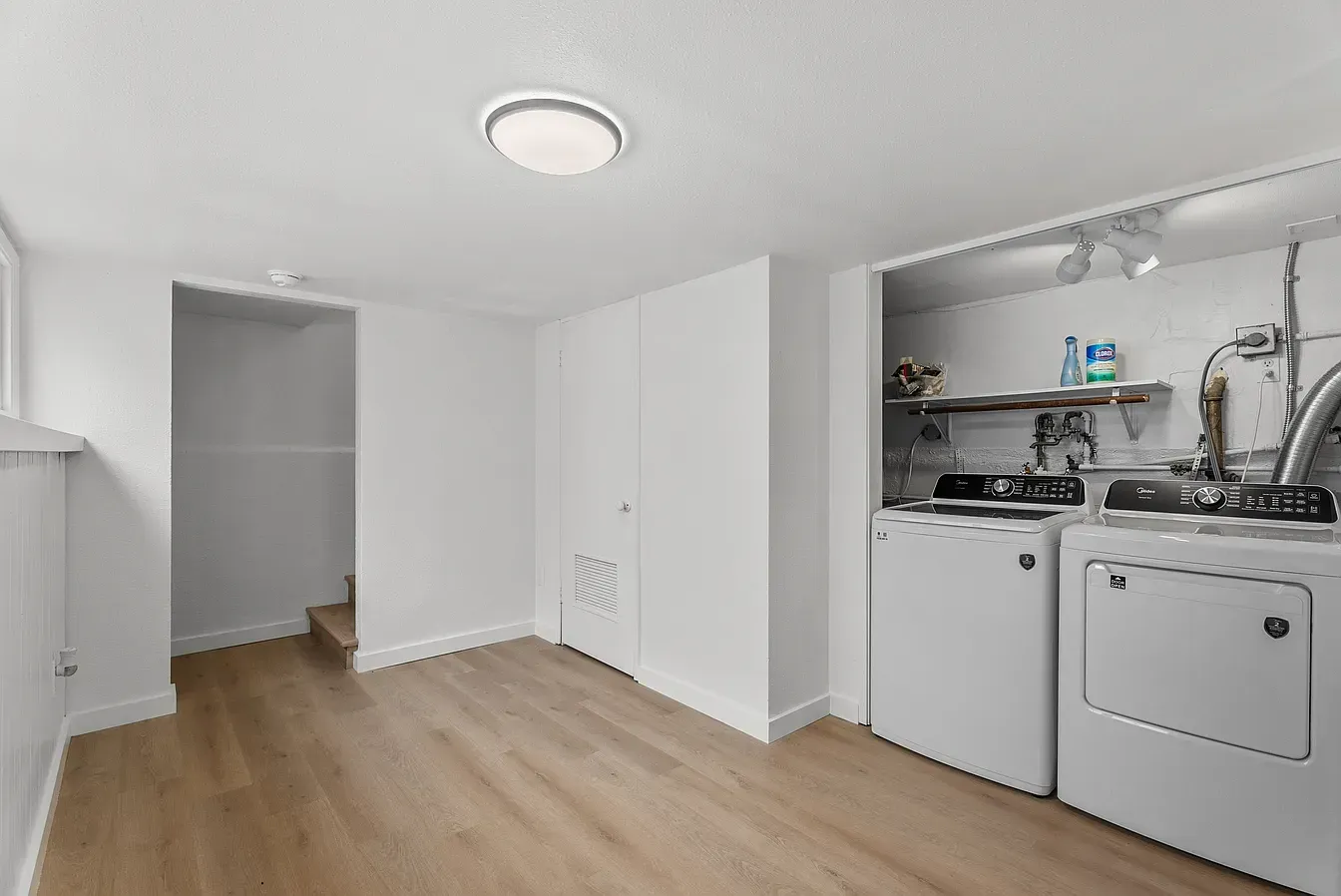 Empty white laundry room with washer, dryer, sink, and light wood floor