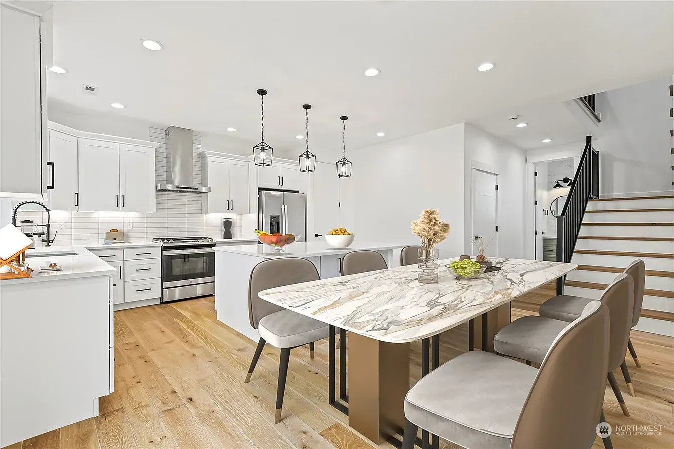 Modern kitchen with white cabinets, island, dining table, and light wood floors.