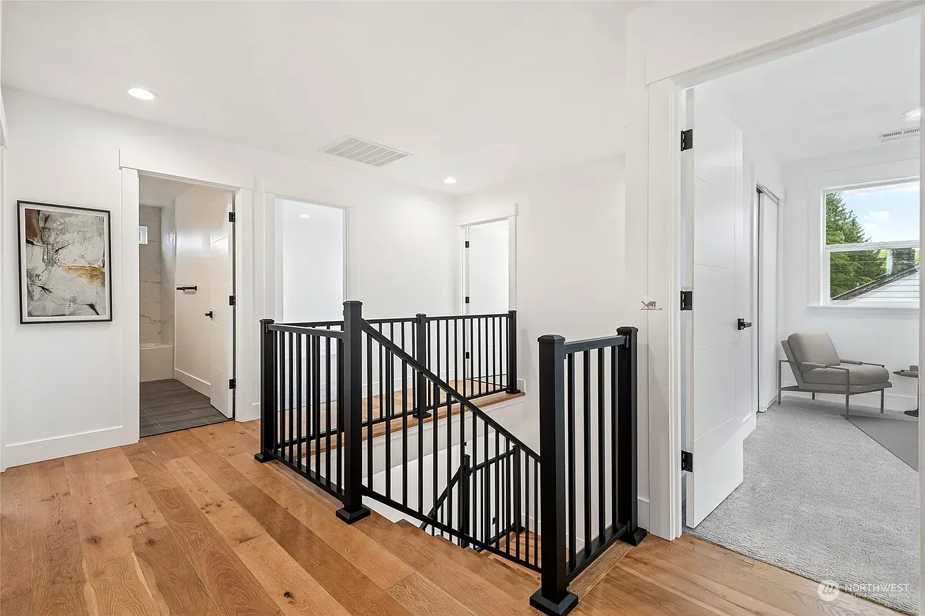 Hallway with black railing, light wood floors, white walls, and open doorways.