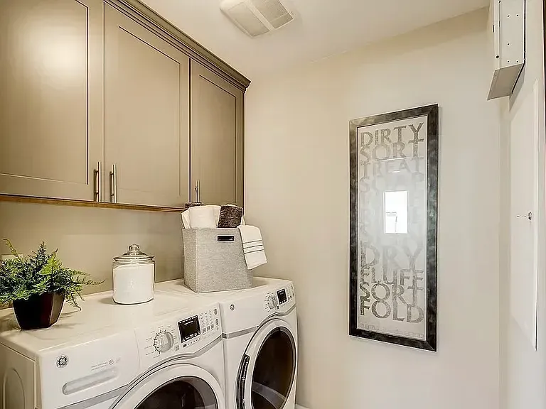 Laundry room with white appliances, gray cabinets, and a framed sign.