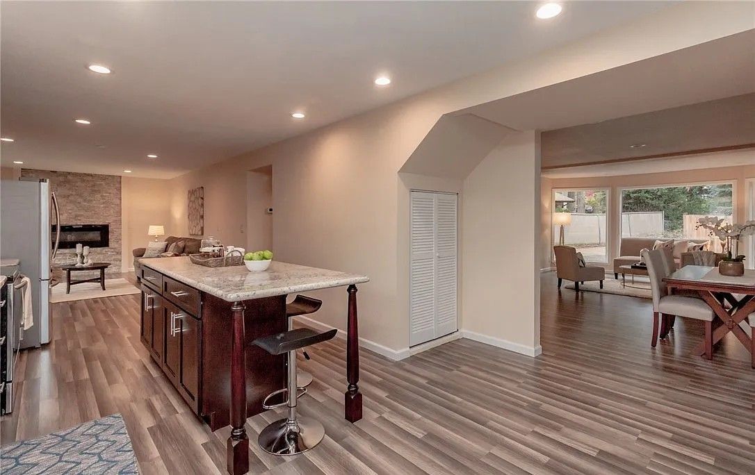 Kitchen with island, opening to living and dining areas; wood floors, neutral walls, recessed lighting.