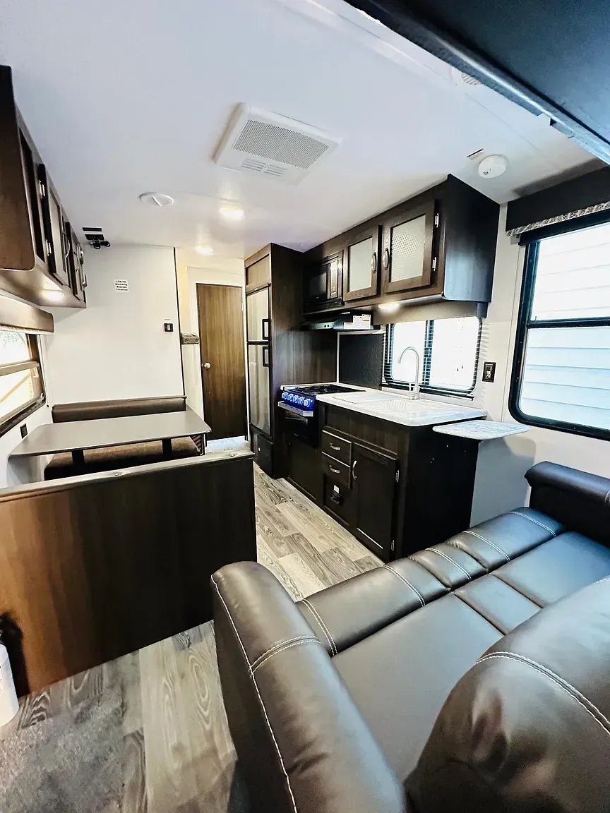 Interior view of a modern RV with dark cabinets, a couch, kitchen, and open layout.
