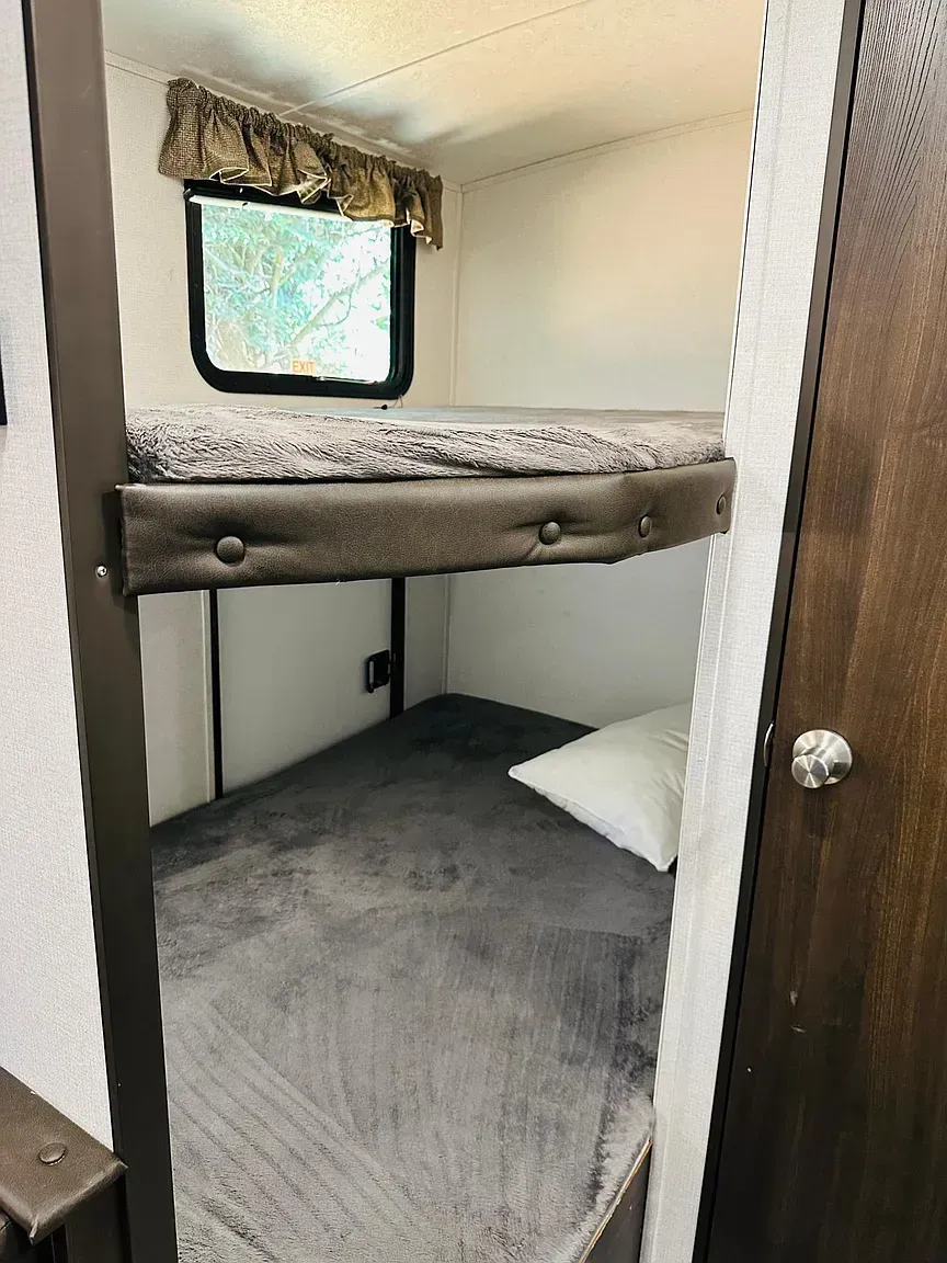 Bunk beds in a small room with a window, dark brown trim, and gray bedding.