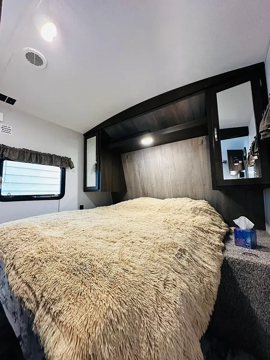 Bedroom in a camper with a large bed covered in a fuzzy blanket, mirrors, and a window.