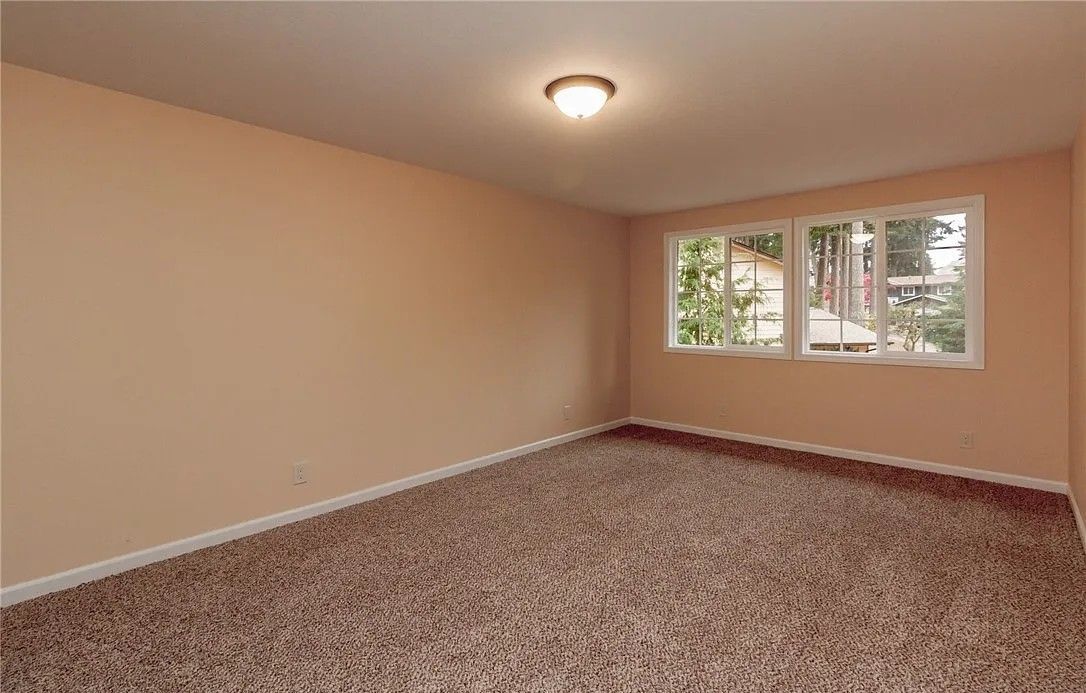 Empty room with beige walls, brown carpet, and a window letting in light.