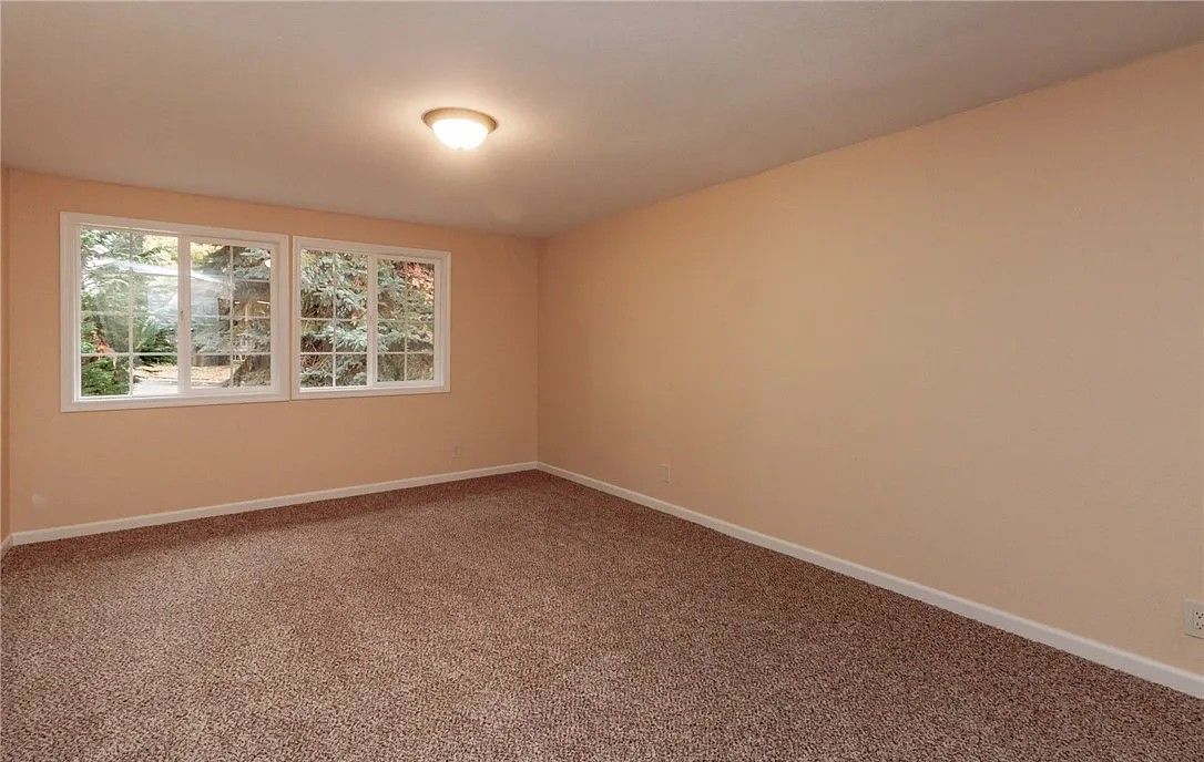 Empty room with beige walls, brown carpet, and a window with a view of greenery.