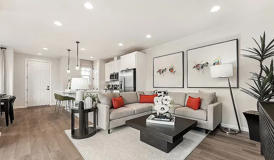 Living room with a gray sectional, red pillows, coffee table, and open kitchen.