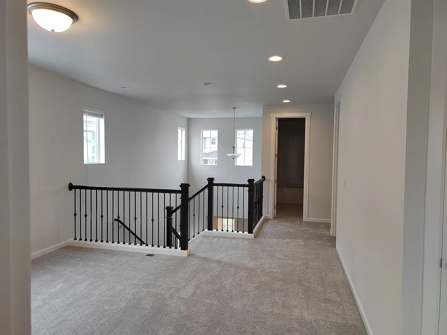Second-floor hallway with carpet, black railing, white walls, recessed lighting, and a door at the end.