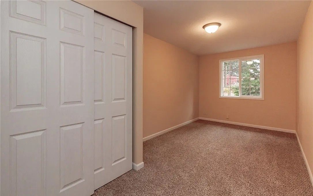 Empty room with a white closet, window, and beige walls, brown carpet.