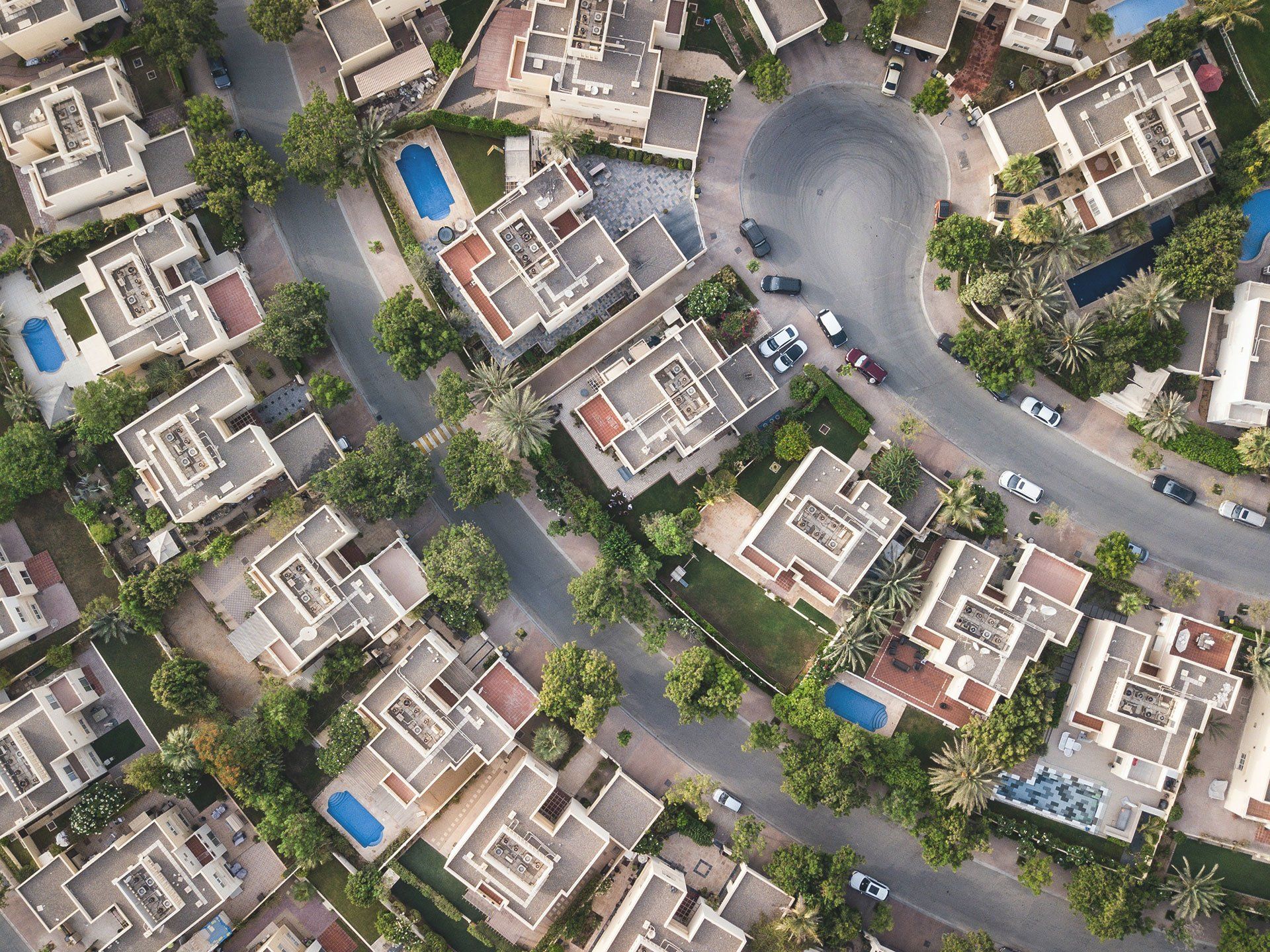 Aerial view of a suburban neighborhood with houses, pools, trees, and winding roads.