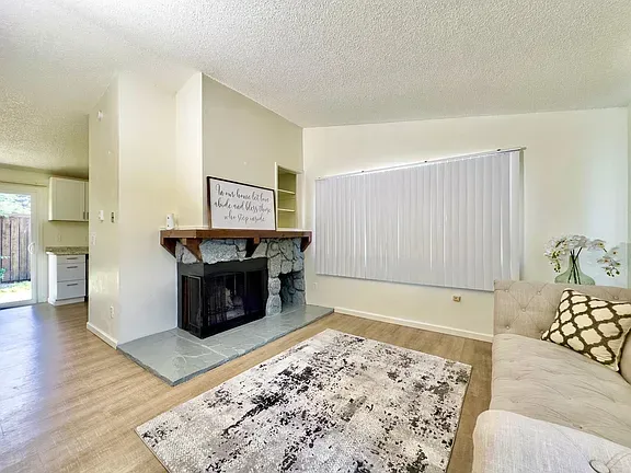 Living room with fireplace, rug, sofa, and a window with blinds.