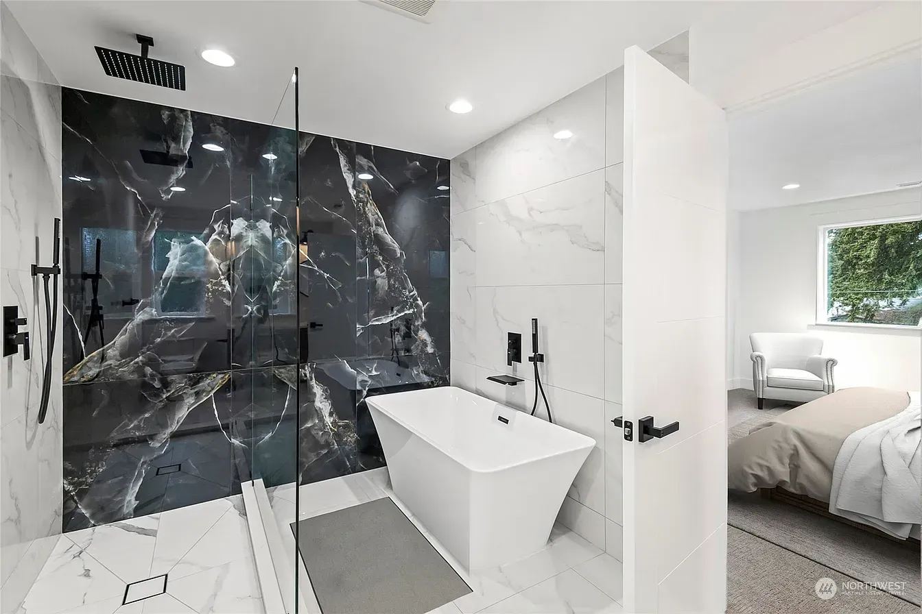 Modern bathroom with black marble shower wall, white tub, and partially visible bedroom.