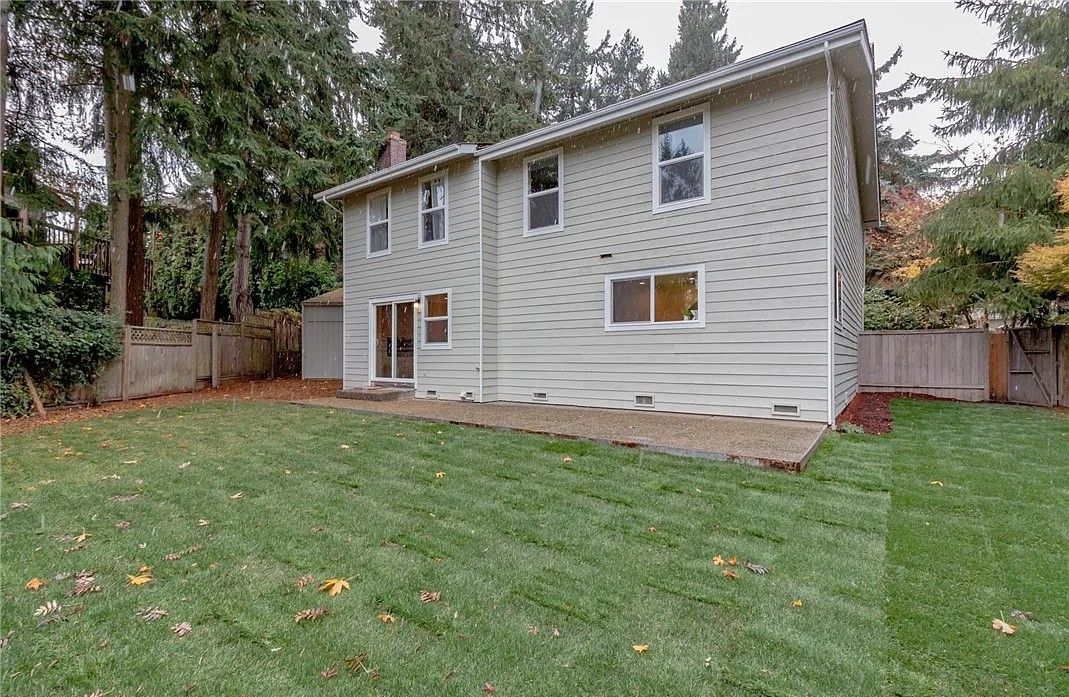 Backyard of a two-story light green house with a grassy lawn and a wooden fence.