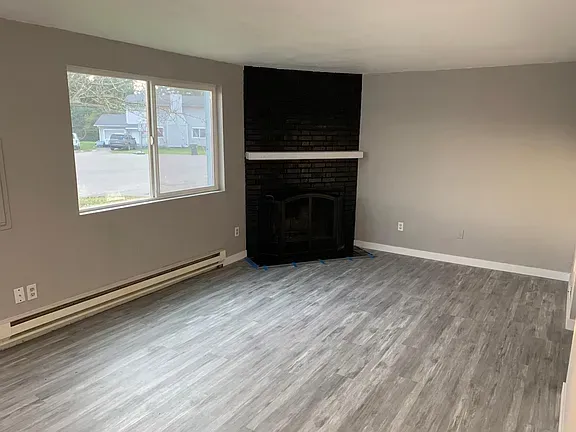 Living room with gray walls, wood-look flooring, fireplace, and window overlooking a street.