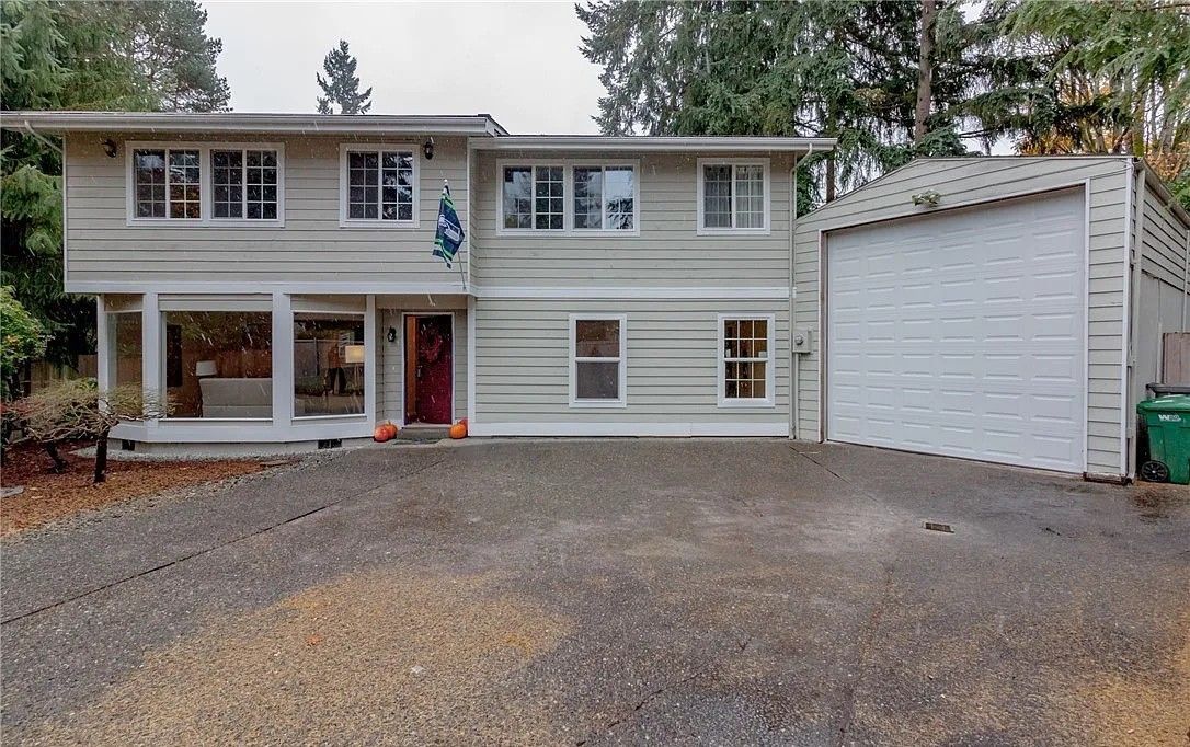 Two-story house with a gravel driveway, attached garage. Light gray exterior, red front door.