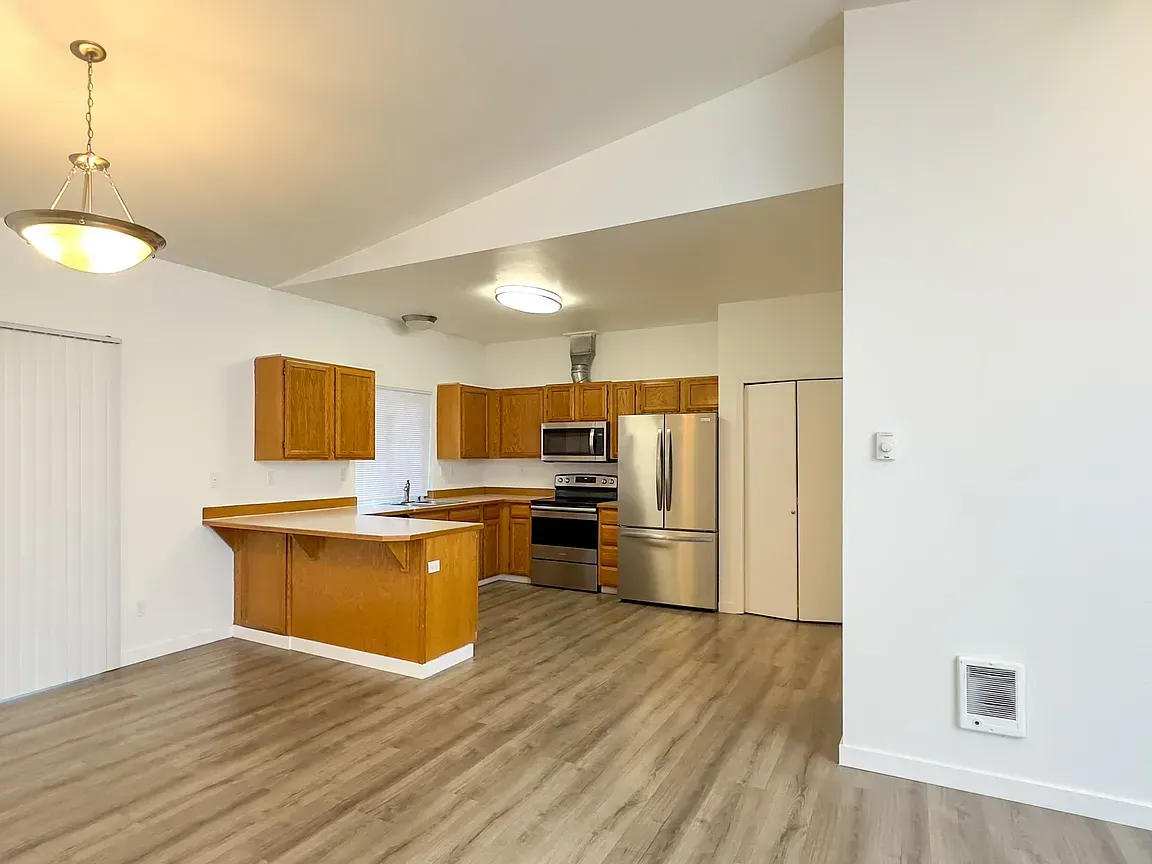 Open-concept kitchen and dining area with wood cabinets, stainless steel appliances, and wood-look flooring.