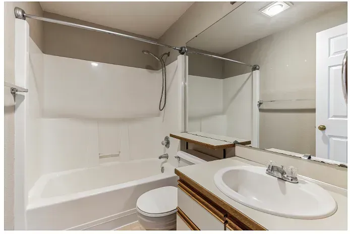 Bathroom with white tub, vanity, and toilet; large mirror; neutral walls.