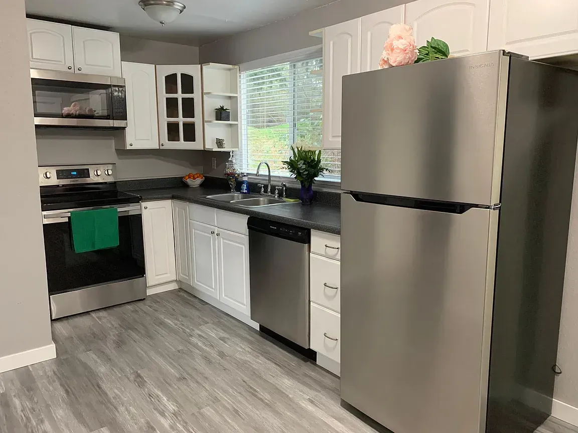 Kitchen with stainless steel appliances, white cabinets, gray walls, and light gray flooring.