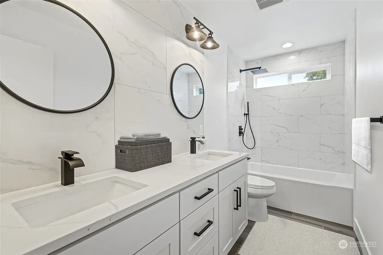 White bathroom with marble-look tile, double vanity, black fixtures, and round mirrors.